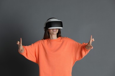 Photo of Smiling woman using virtual reality headset on gray background