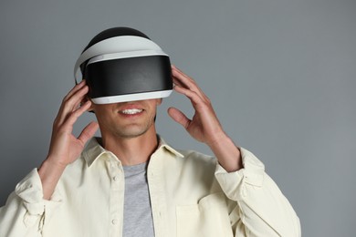 Photo of Smiling man using virtual reality headset on gray background, space for text
