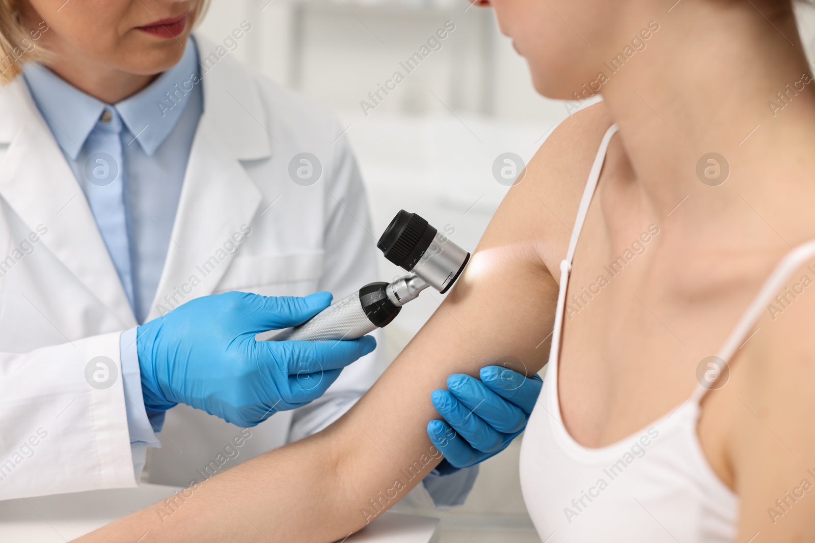 Photo of Dermatologist with dermatoscope examining patient in clinic, closeup