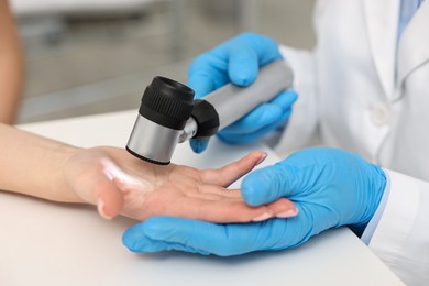 Dermatologist with dermatoscope examining patient at white table in clinic, closeup