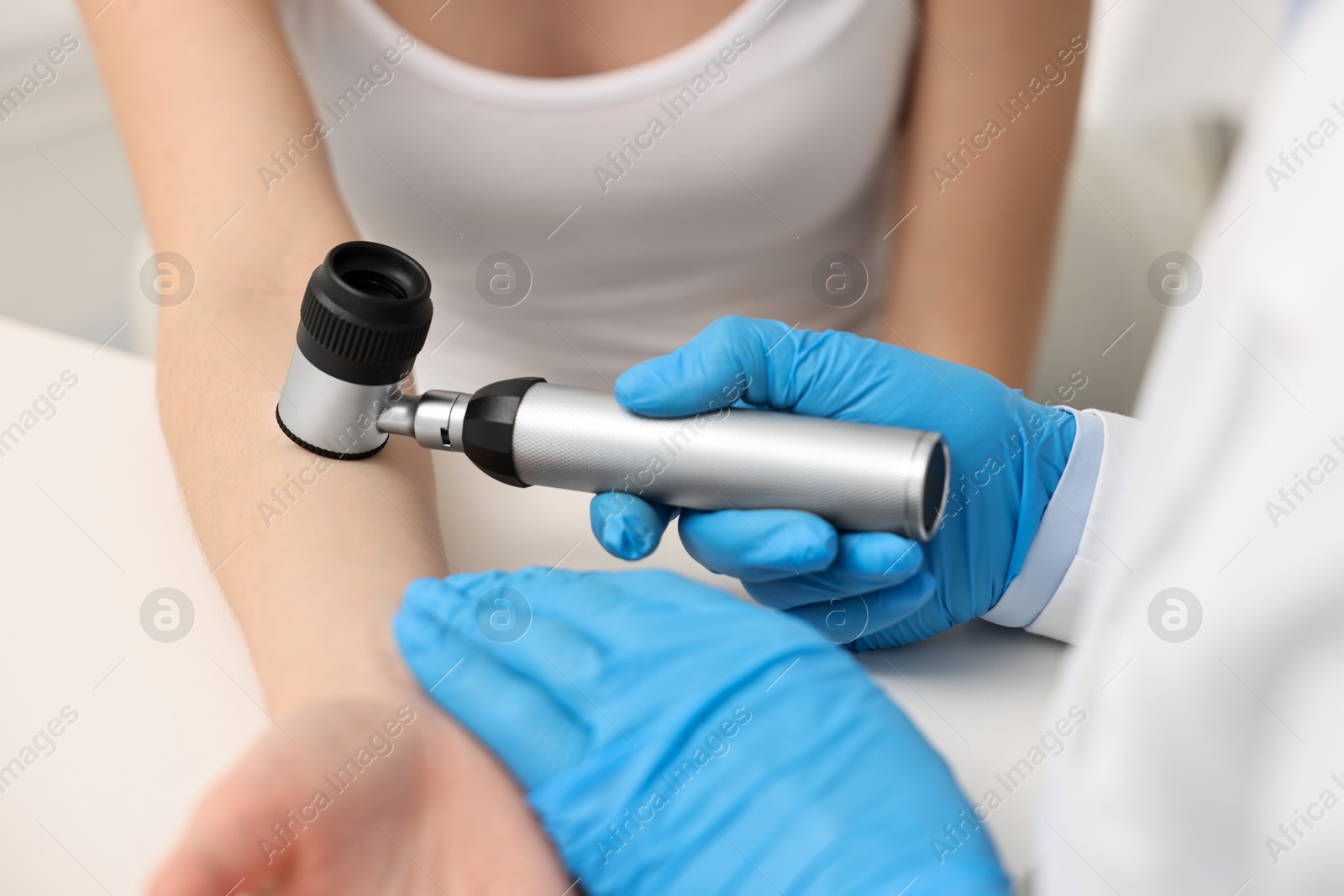 Photo of Dermatologist with dermatoscope examining patient at white table in clinic, closeup