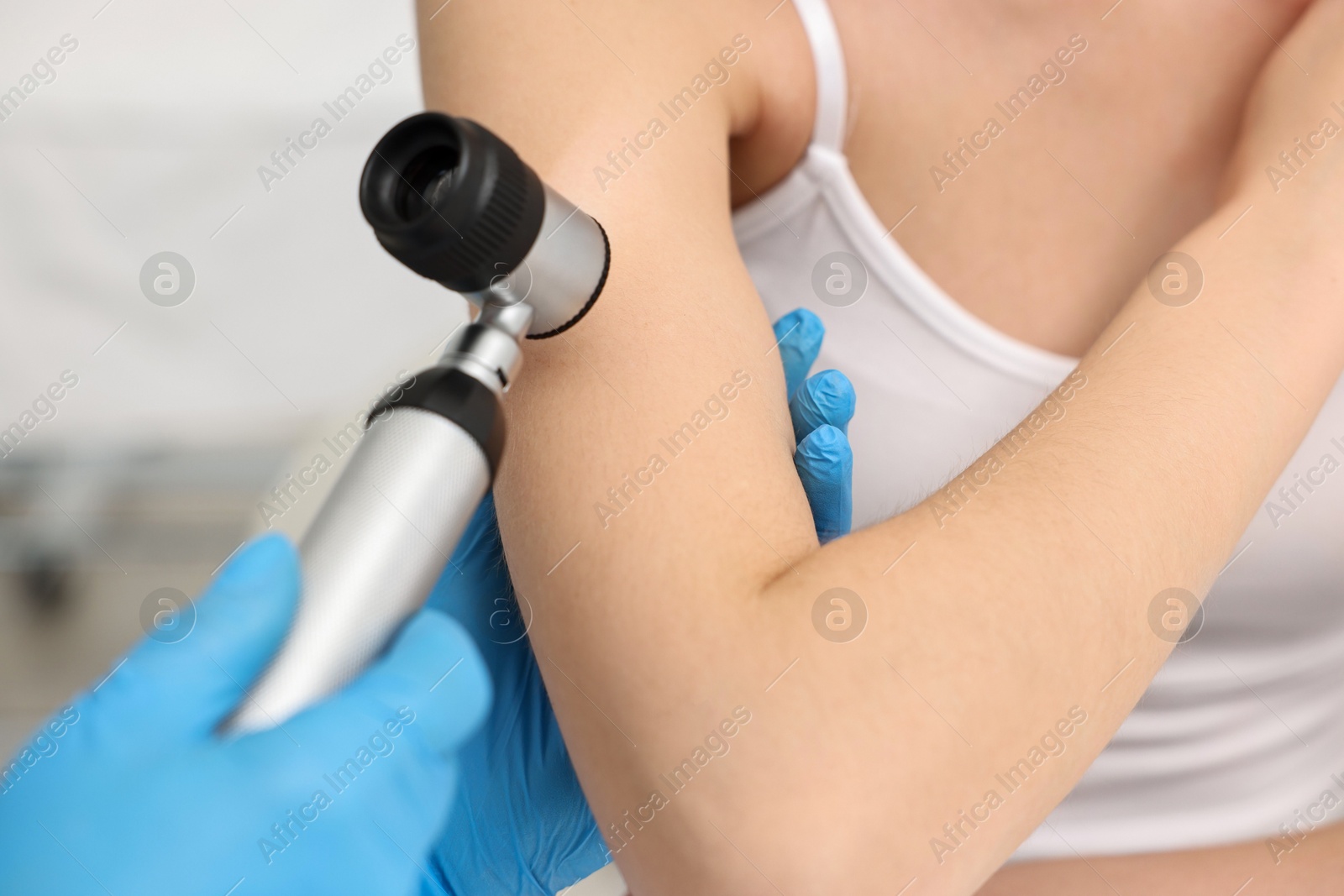 Photo of Dermatologist with dermatoscope examining patient in clinic, closeup