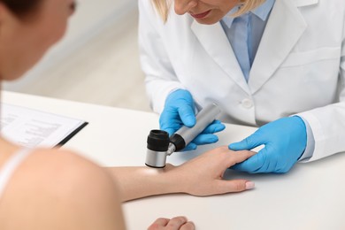 Dermatologist with dermatoscope examining patient at white table in clinic, closeup