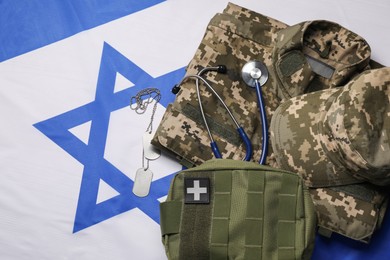 Stethoscope, first aid kit, tags and military uniform on flag of Israel, flat lay