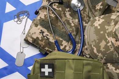 Stethoscope, first aid kit, tags and military uniform on flag of Israel, flat lay