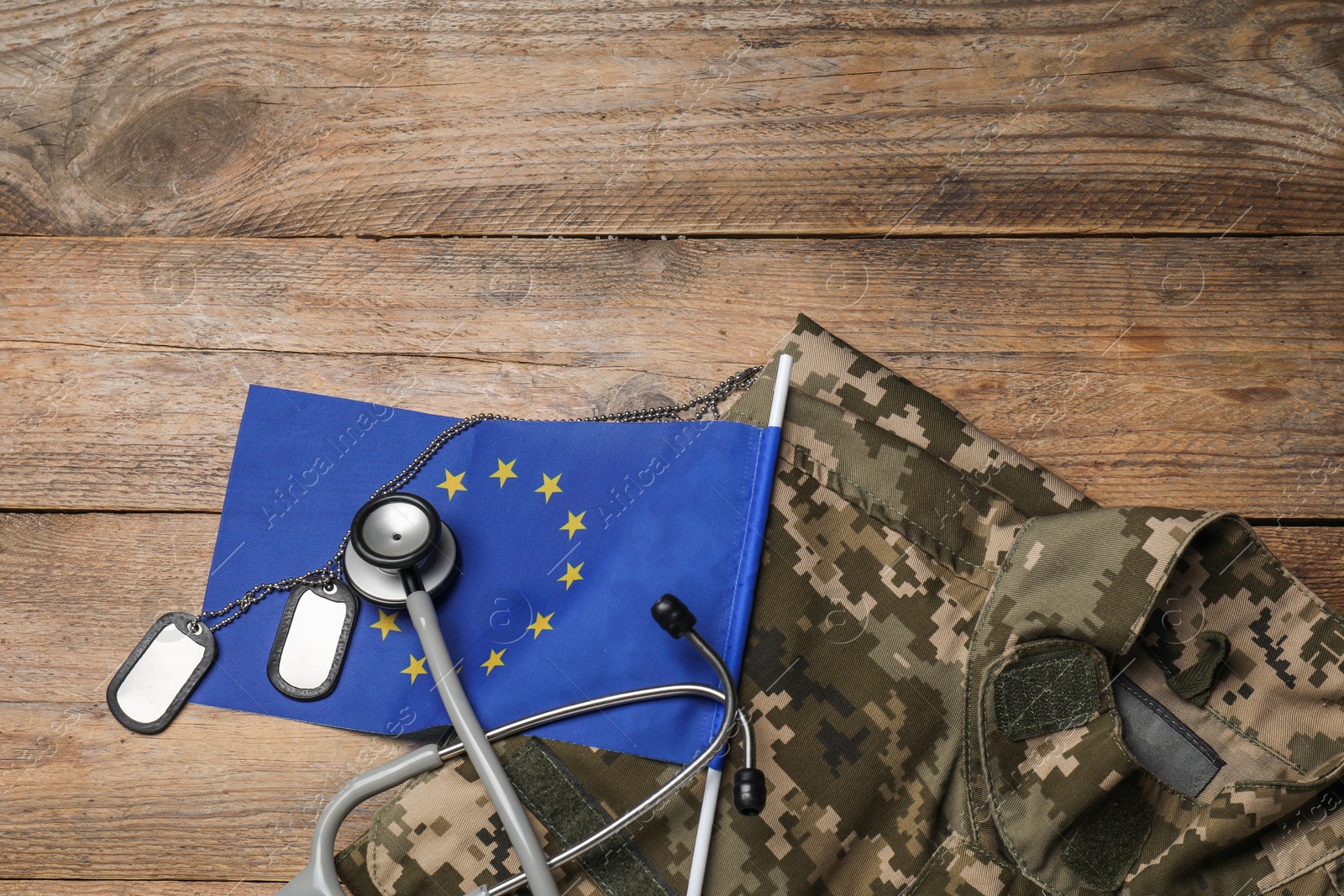 Photo of Stethoscope, flag of European Union, tags and military uniform on wooden table, flat lay. Space for text