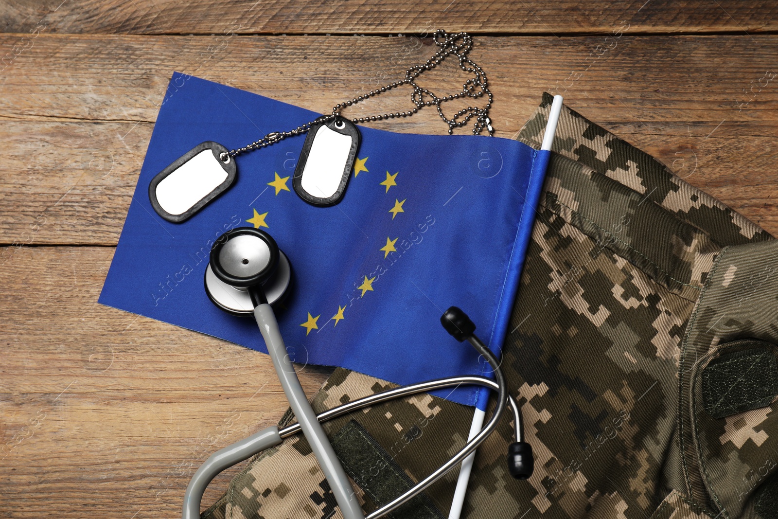 Photo of Stethoscope, flag of European Union, tags and military uniform on wooden table, flat lay