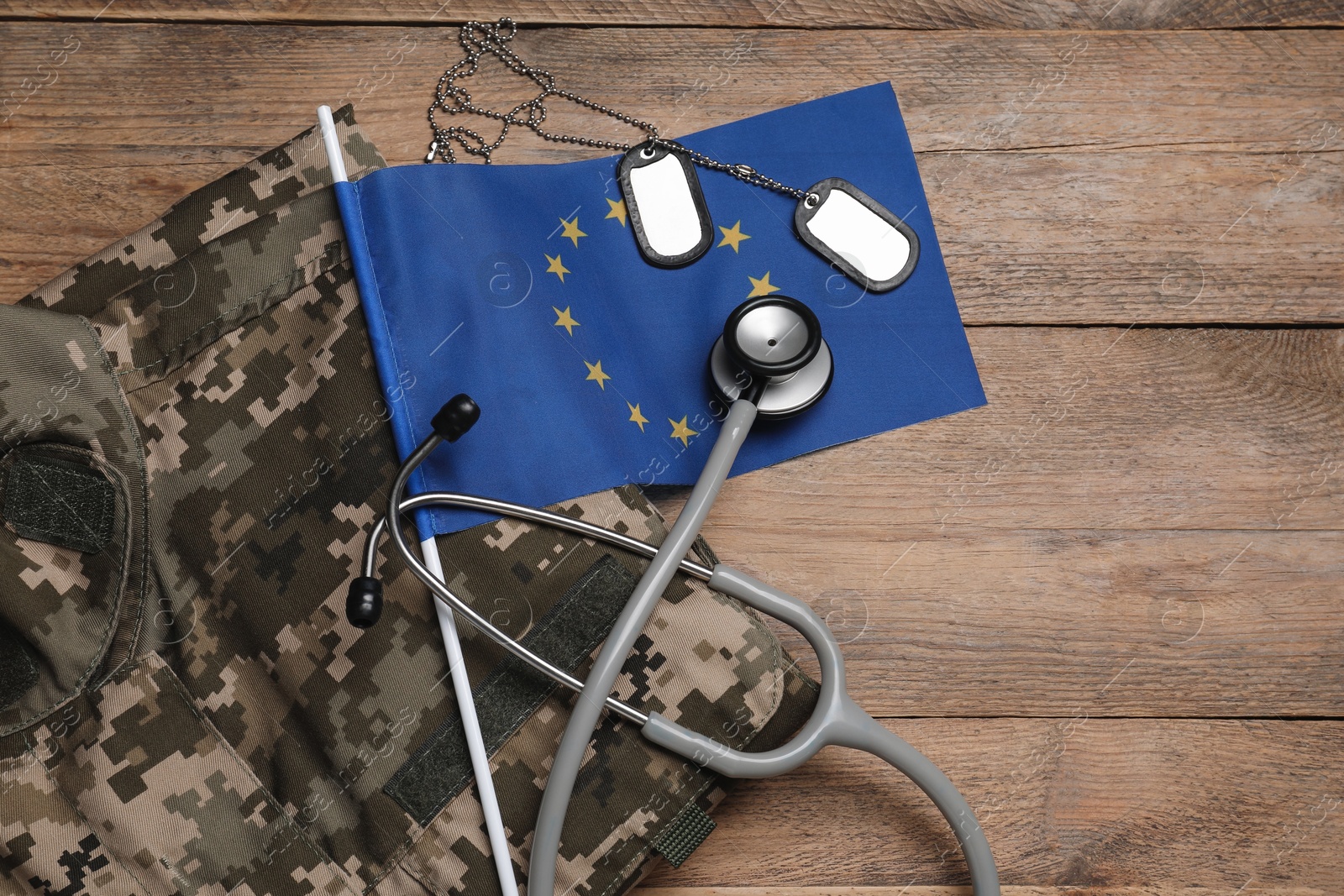 Photo of Stethoscope, flag of European Union, tags and military uniform on wooden table, flat lay. Space for text