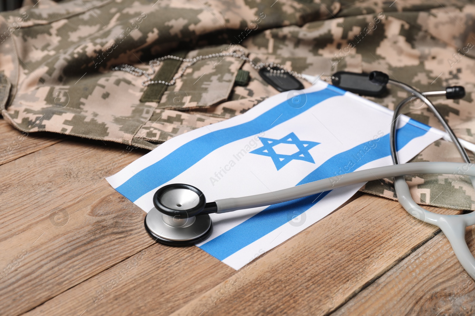 Photo of Stethoscope, flag of Israel, tags and military uniform on wooden table, closeup