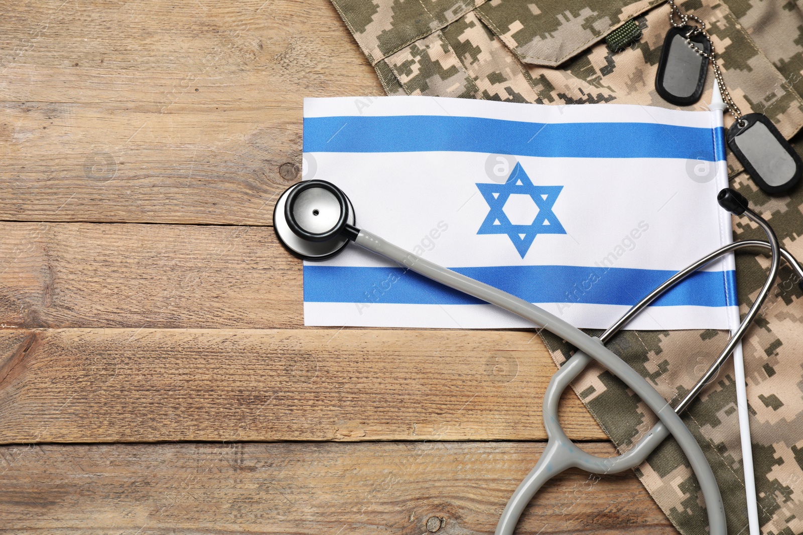 Photo of Stethoscope, flag of Israel, tags and military uniform on wooden table, flat lay. Space for text