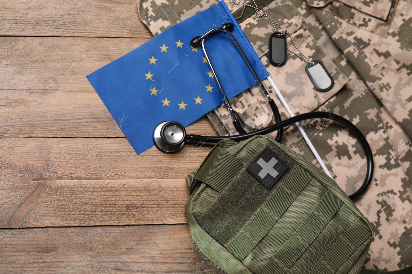 Photo of Stethoscope, flag of European Union, first aid kit and military uniform on wooden table, flat lay. Space for text