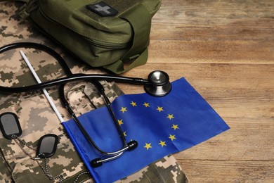 Photo of Stethoscope, flag of European Union, first aid kit and military uniform on wooden table
