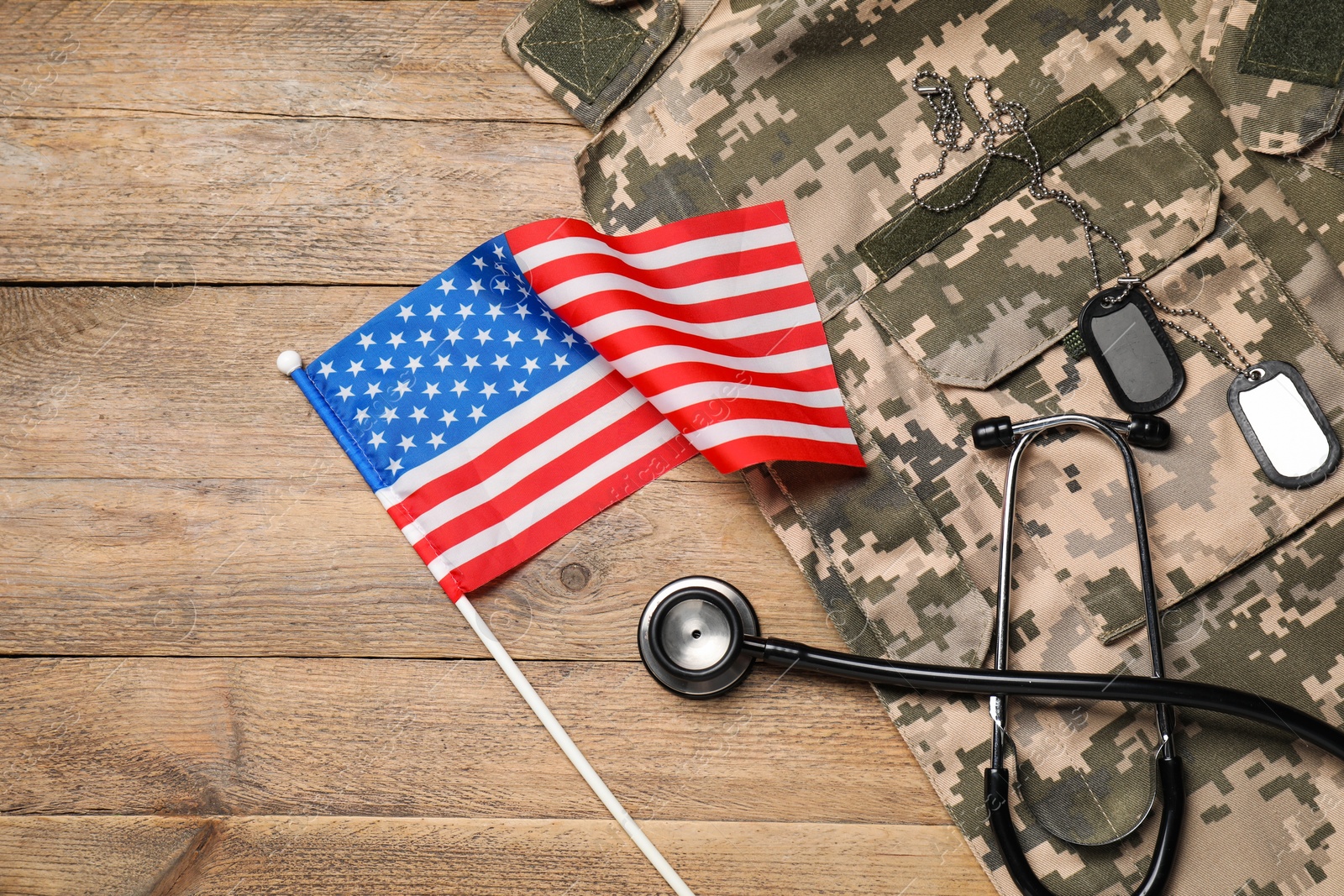 Photo of Stethoscope, USA flag, tags and military uniform on wooden table, flat lay