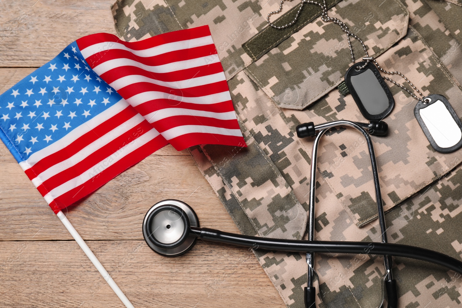 Photo of Stethoscope, USA flag, tags and military uniform on wooden table, flat lay