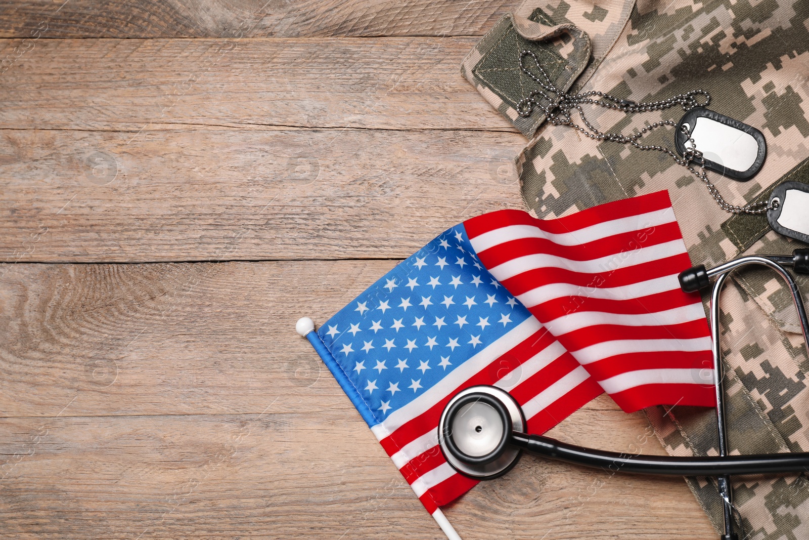 Photo of Stethoscope, USA flag, tags and military uniform on wooden table, flat lay. Space for text