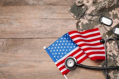 Photo of Stethoscope, USA flag, tags and military uniform on wooden table, flat lay. Space for text