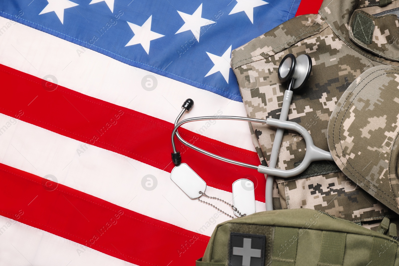 Photo of Stethoscope, first aid kit, tags and military uniform on USA flag, top view
