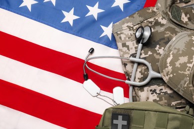 Photo of Stethoscope, first aid kit, tags and military uniform on USA flag, top view