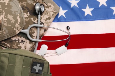 Stethoscope, first aid kit, tags and military uniform on USA flag, top view