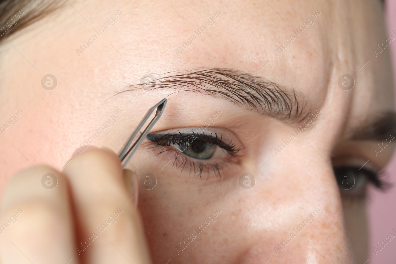 Photo of Young woman plucking eyebrow with tweezers, closeup