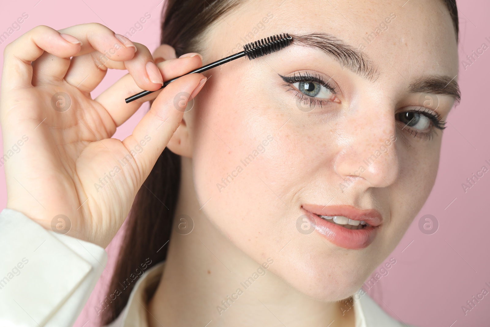 Photo of Young woman brushing eyebrow on pink background, closeup