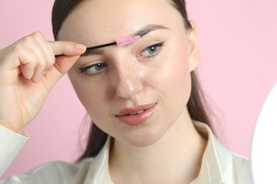 Young woman brushing eyebrow on pink background, closeup