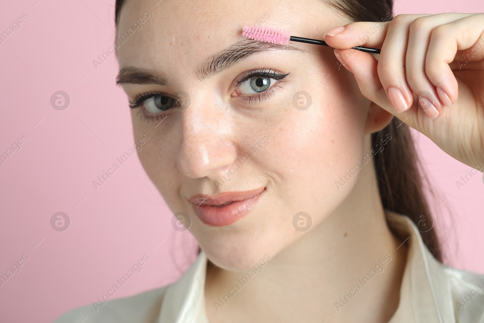 Photo of Young woman brushing eyebrow on pink background, closeup