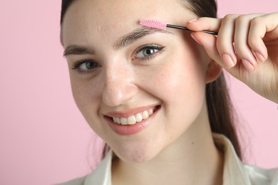 Young woman brushing eyebrow on pink background, closeup