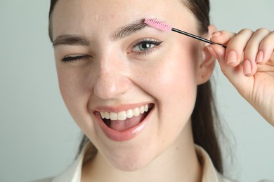 Young woman with spoolie brush on light background, closeup. Eyebrow correction