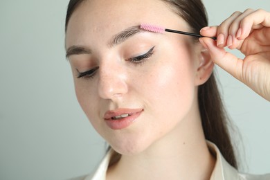 Young woman with spoolie brush on light background, closeup. Eyebrow correction