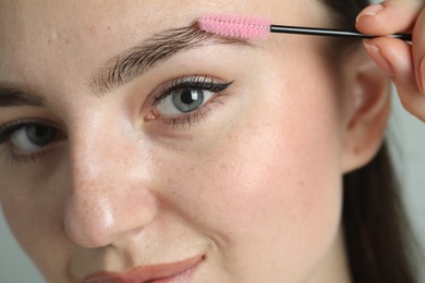 Photo of Young woman with spoolie brush on light background, closeup. Eyebrow correction