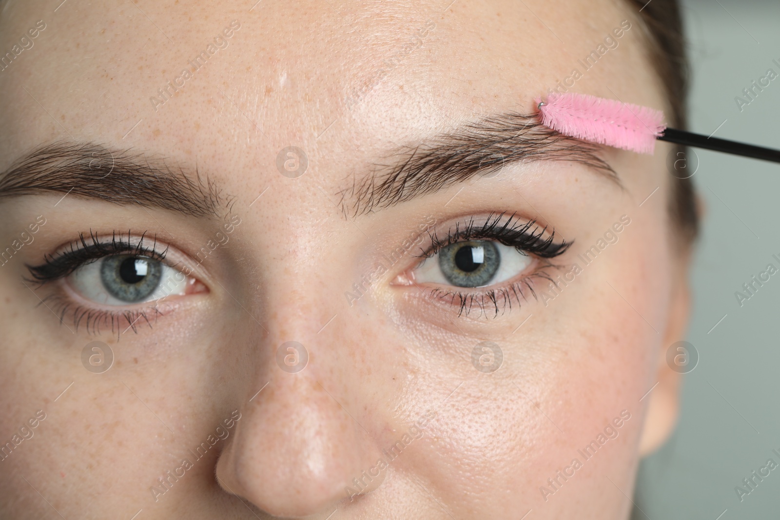 Photo of Young woman with spoolie brush on light background, closeup. Eyebrow correction