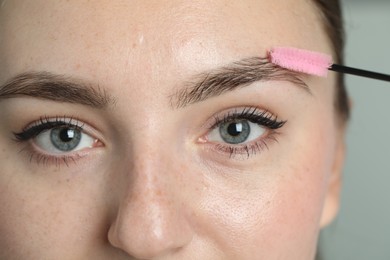 Photo of Young woman with spoolie brush on light background, closeup. Eyebrow correction