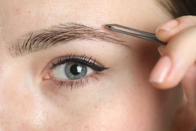 Photo of Young woman plucking eyebrow with tweezers, closeup