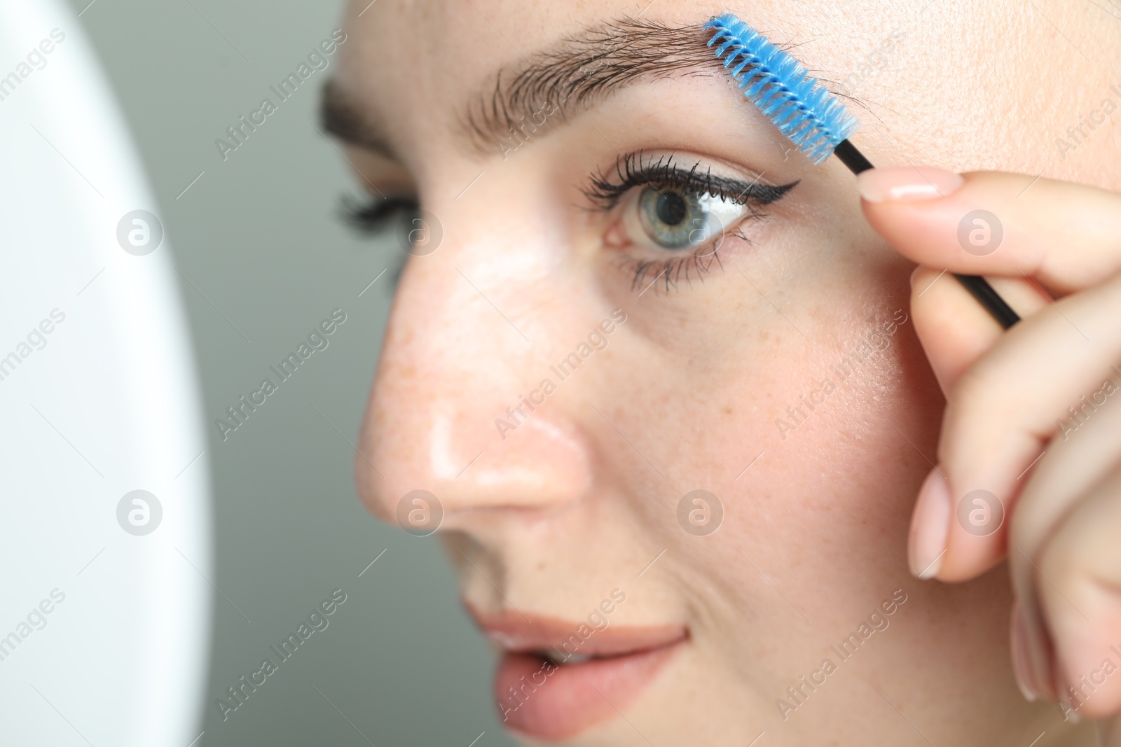 Photo of Young woman with spoolie brush on light background, closeup. Eyebrow correction