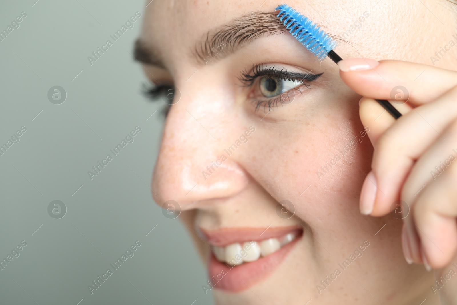 Photo of Young woman with spoolie brush on light background, closeup. Eyebrow correction