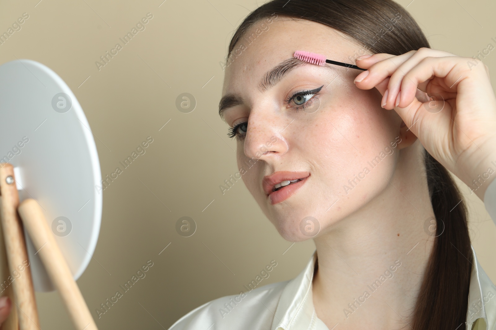 Photo of Young woman with spoolie brush on beige background, closeup. Eyebrow correction