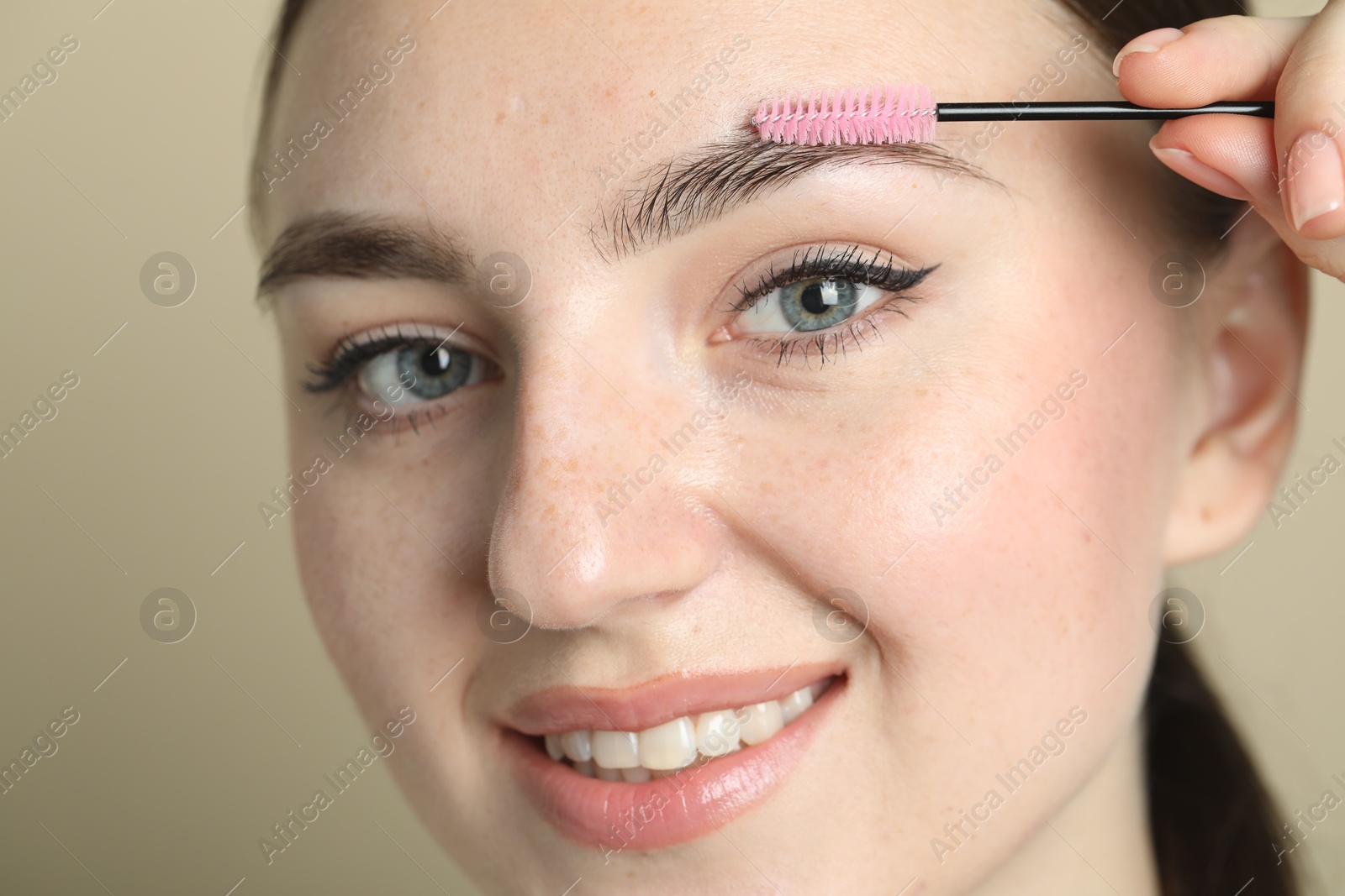 Photo of Young woman with spoolie brush on beige background, closeup. Eyebrow correction