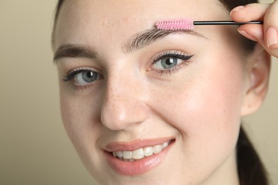 Young woman with spoolie brush on beige background, closeup. Eyebrow correction