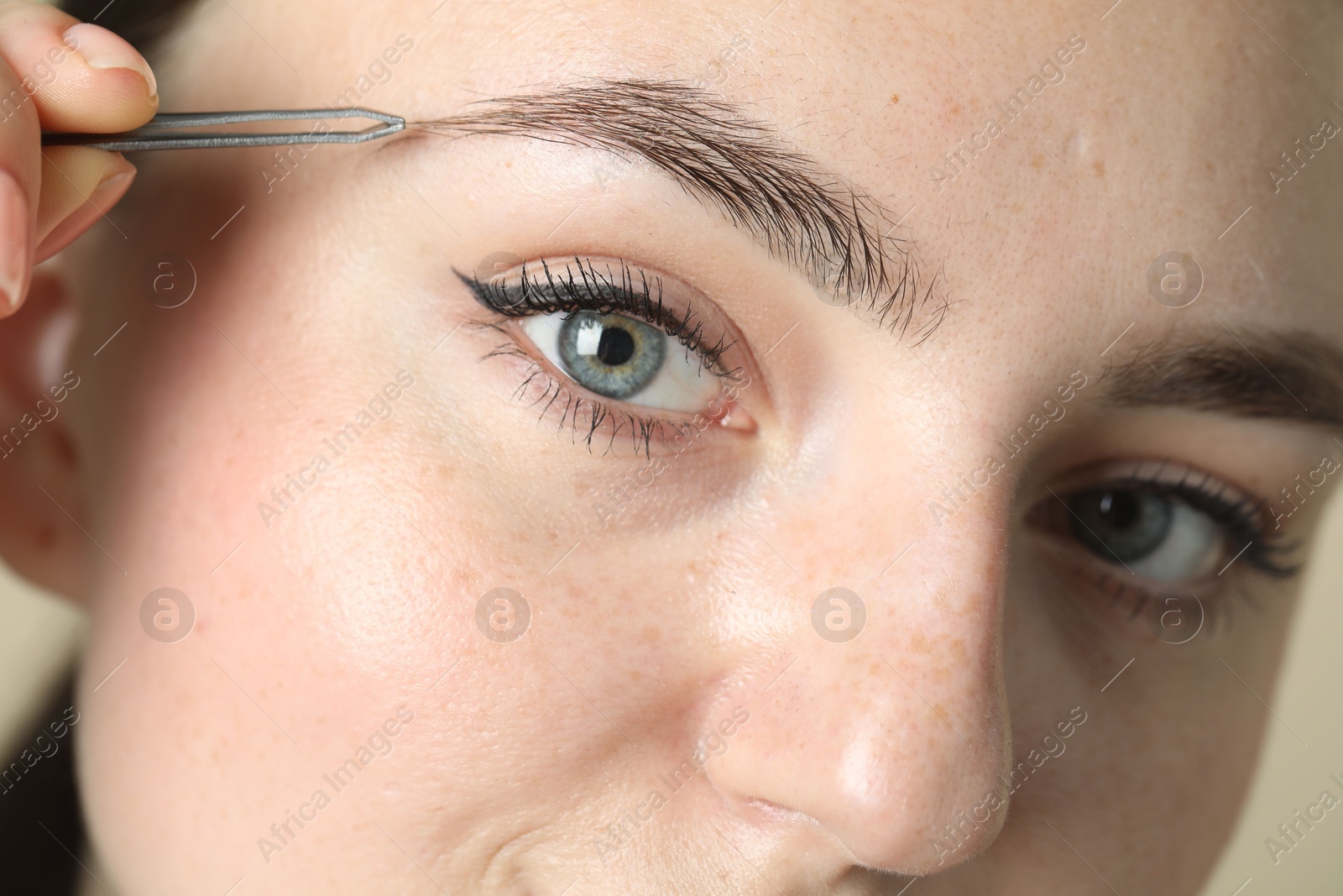 Photo of Young woman plucking eyebrow with tweezers, closeup