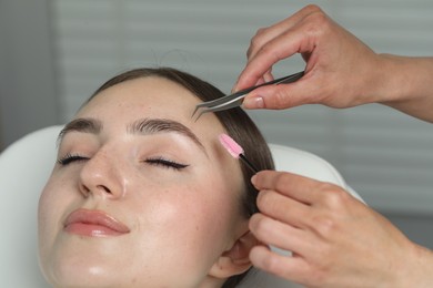 Photo of Beautician making eyebrow correction to young woman in beauty salon, closeup