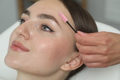 Photo of Beautician brushing young woman's eyebrow in beauty salon, closeup