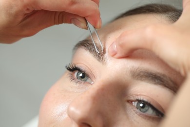 Photo of Beautician plucking young woman's eyebrow on light background, closeup