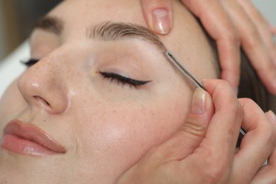 Beautician plucking young woman's eyebrow, closeup view