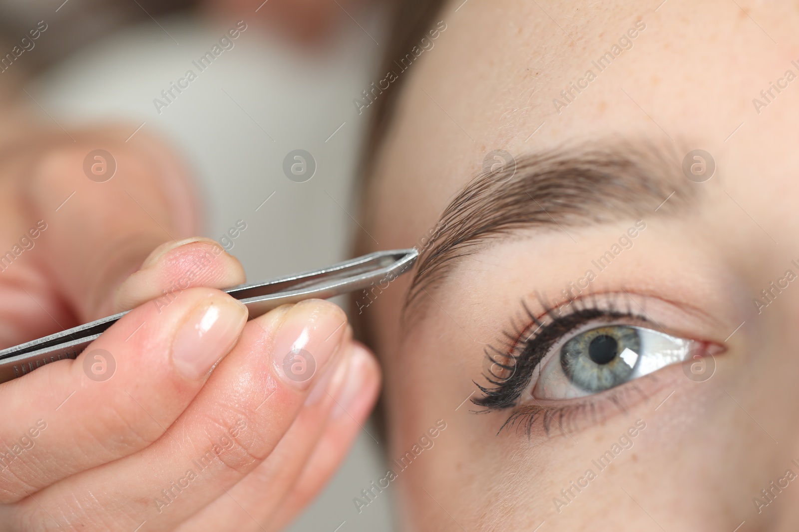 Photo of Beautician plucking young woman's eyebrow in beauty salon, closeup