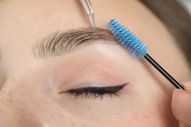 Photo of Beautician making eyebrow correction to young woman, closeup