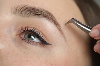 Beautician plucking young woman's eyebrow, closeup view