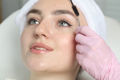 Beautician making eyebrow correction to young woman in beauty salon, closeup