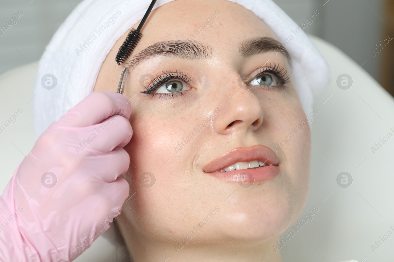 Photo of Beautician making eyebrow correction to young woman in beauty salon, closeup