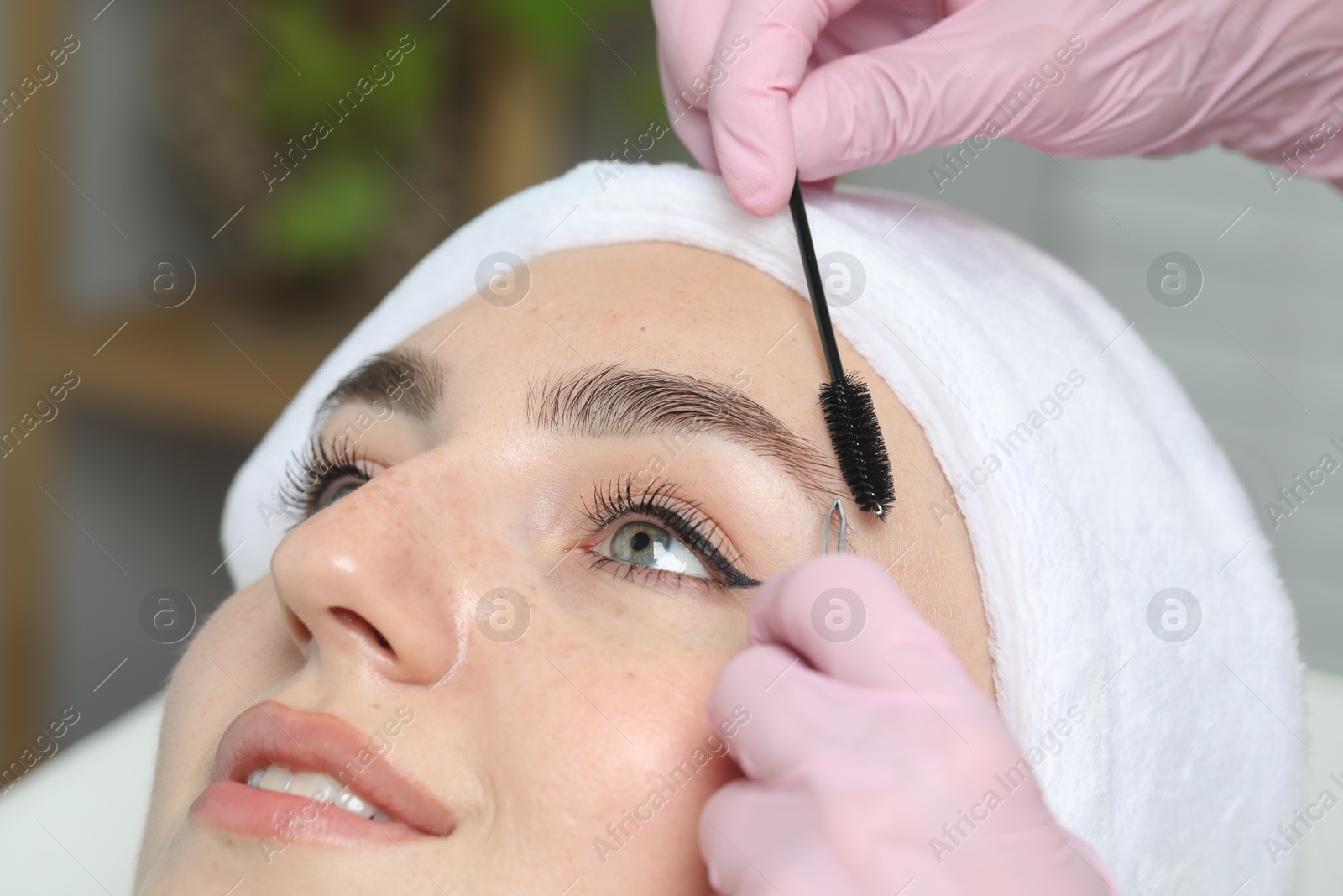 Photo of Beautician making eyebrow correction to young woman in beauty salon, closeup